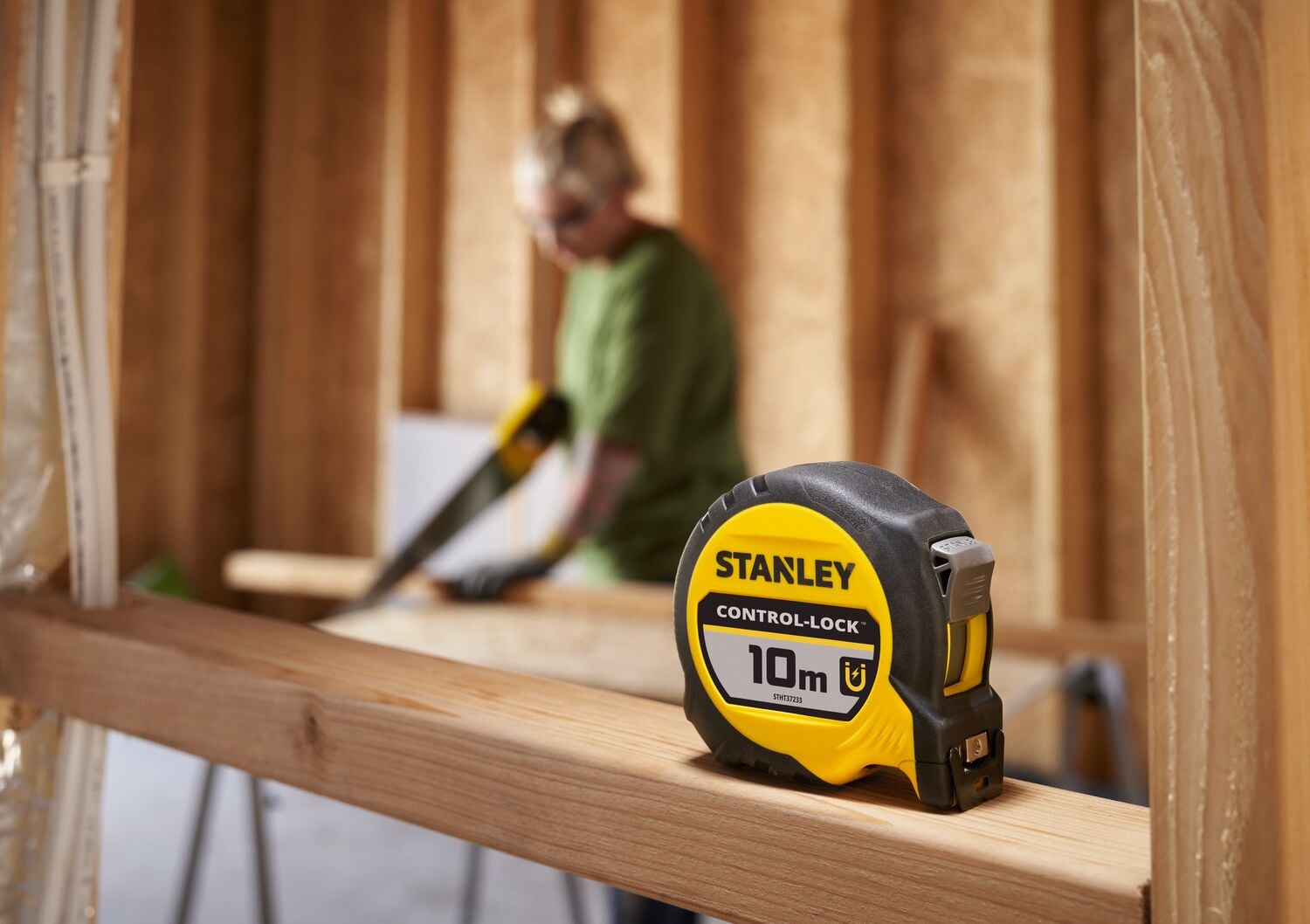 STANLEY® CONTROL-LOCK™ 10M (25mm wide) Tape Measure sitting on timber frame, worker on site in background.