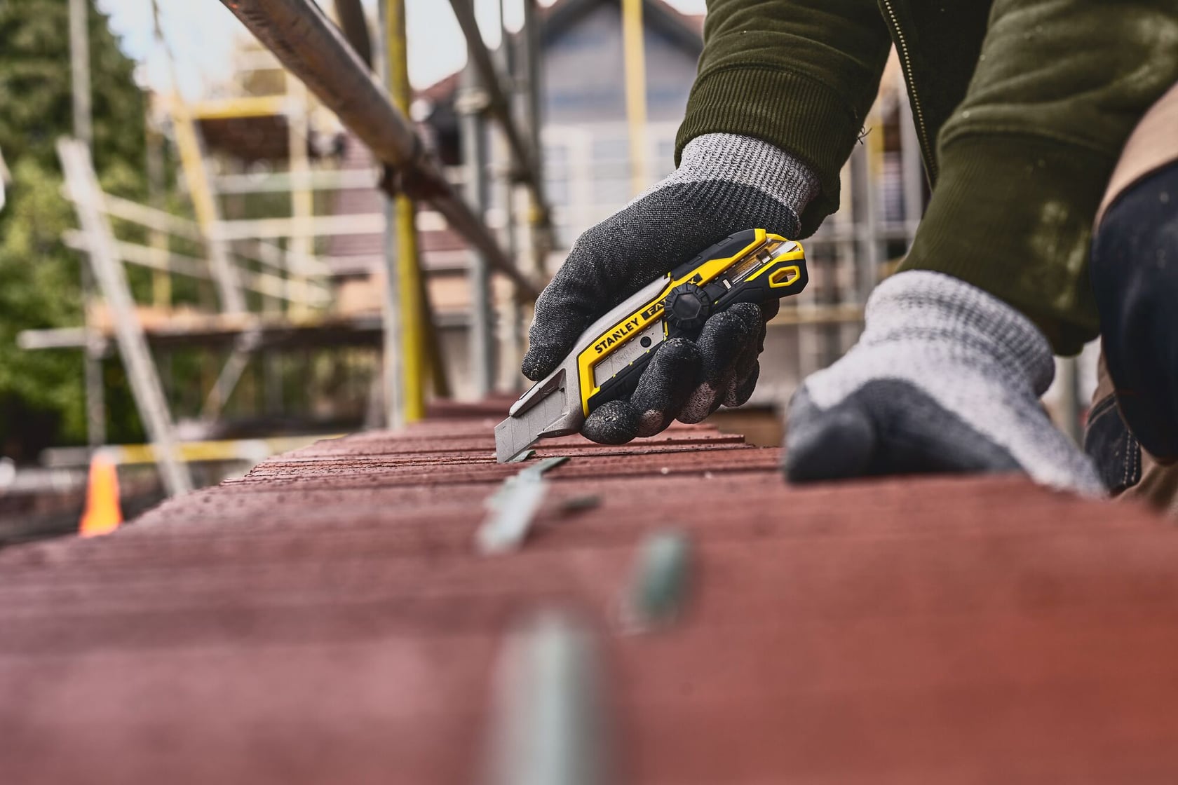 Cutter STANLEY FMHT10592-0 dans une main gantée, coupant sur une surface rouge, en extérieur sur un chantier.